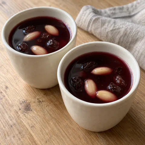 Mörkröd hemgjord glögg med russin och skållad mandel i små vita koppar