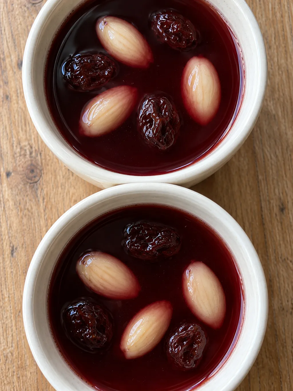 Två koppar mörkröd glögg med ljus mandel och russin på ett träbord
