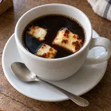 Kopp med mörkt kaffe och små bitar brunfläckig kaffeost.