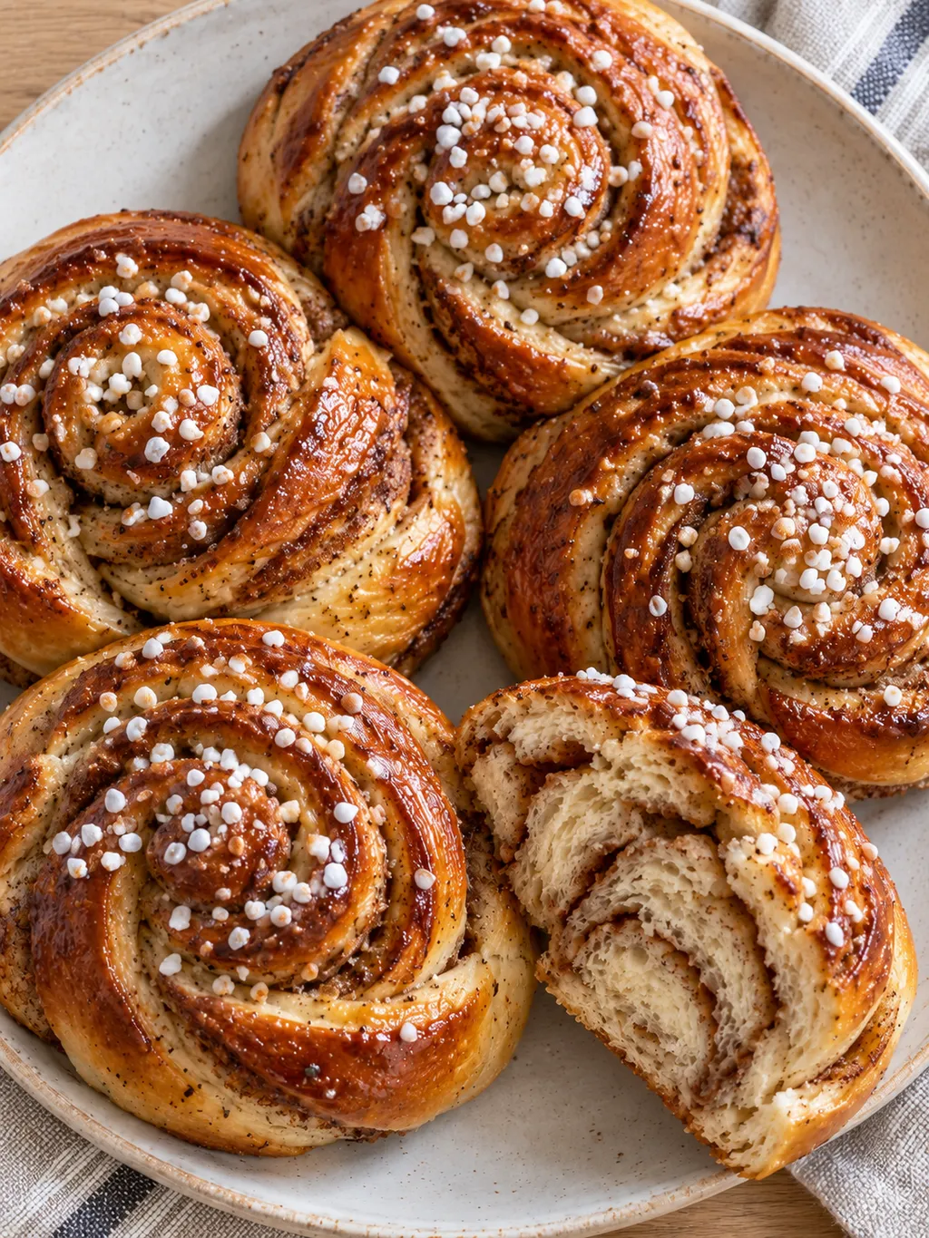 Kanelbullar med kardemumma och pärlsocker tätt placerade på ett ljust fat