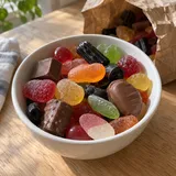 En liten skål med blandat godis och en öppen papperspåse på ett köksbord.