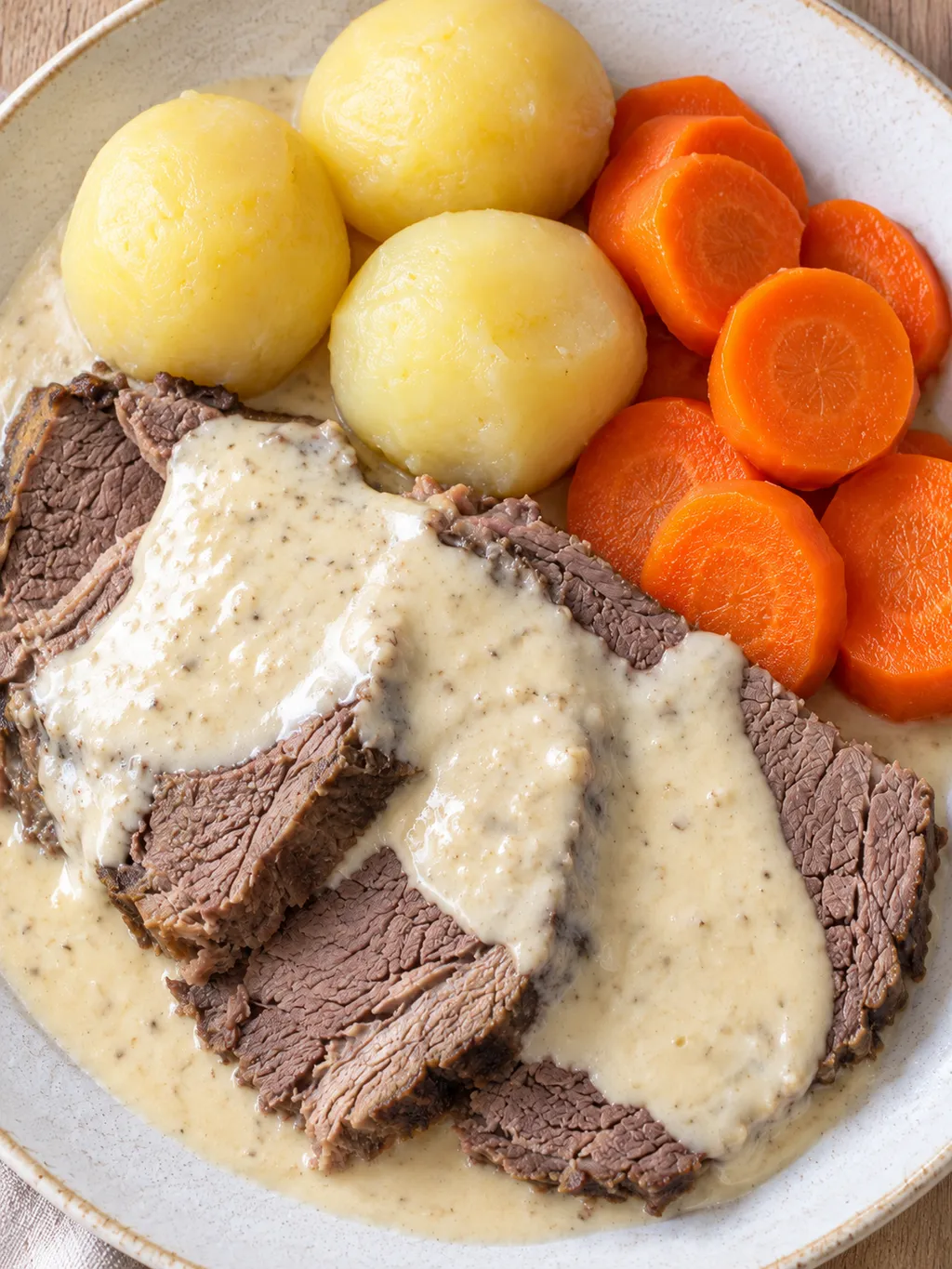 Skivat pepparrotskött med gräddig pepparrotssås, potatis och morötter på ljus tallrik